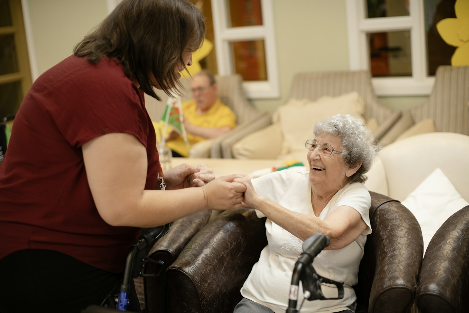 A carer warmly holding hands with an elderly client by her walking frame, supporting her recovery